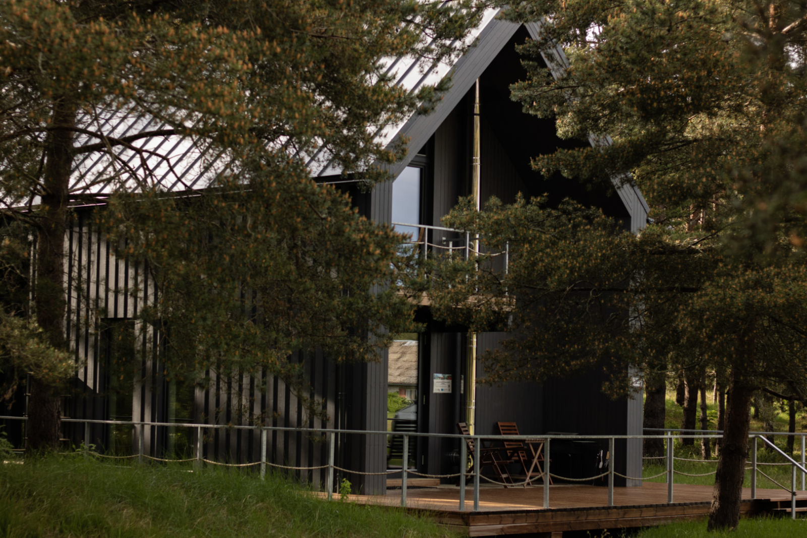 Brūna divstāvīga viesu māja ar gaismu logos aiz priežu zariem