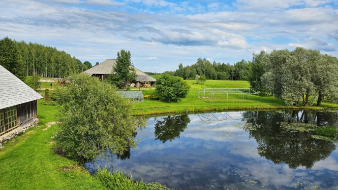 Lauku māja ar dīķi priekšplānā un kokiem apkārt