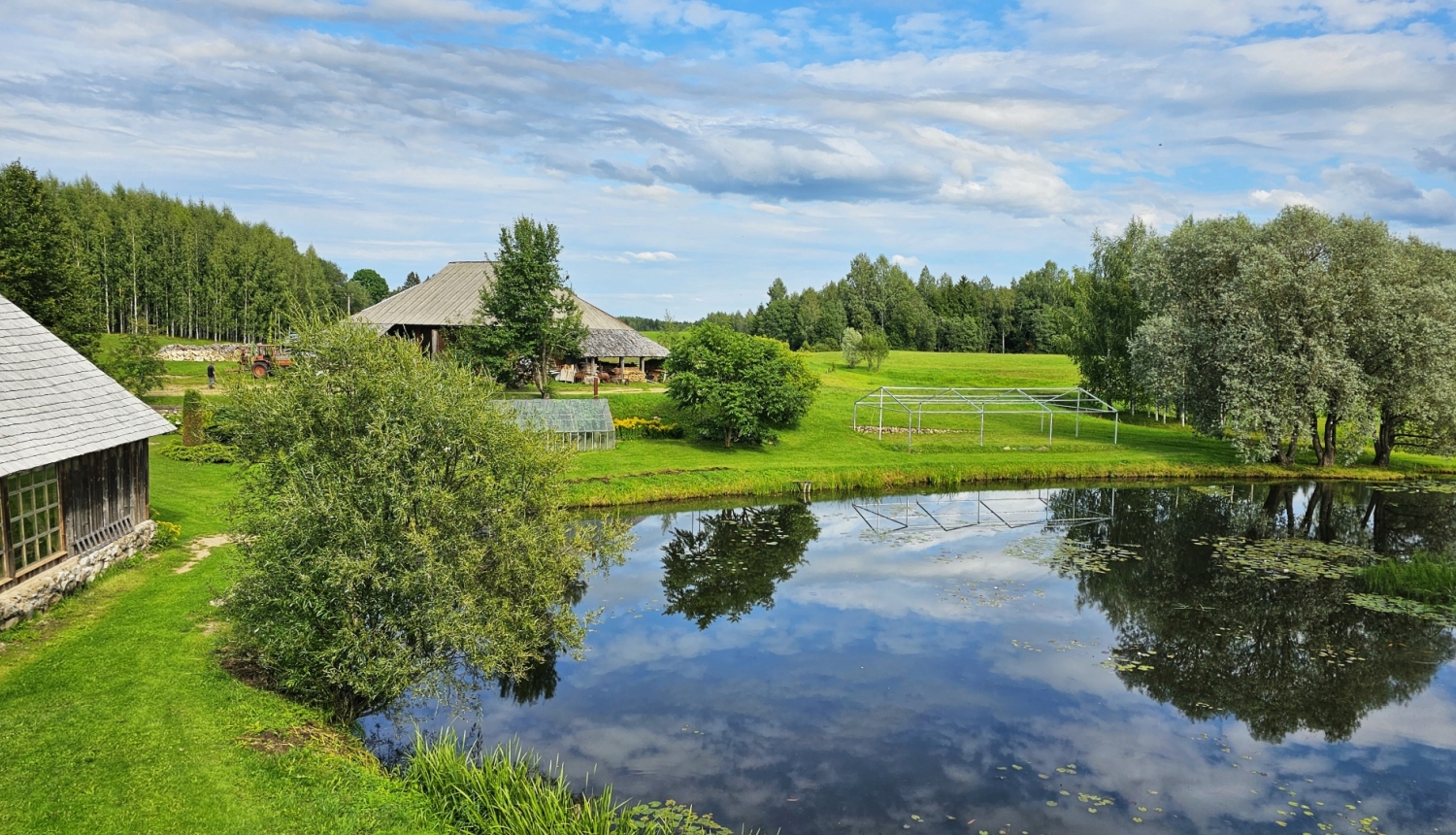 Lauku māja ar dīķi priekšplānā un kokiem apkārt