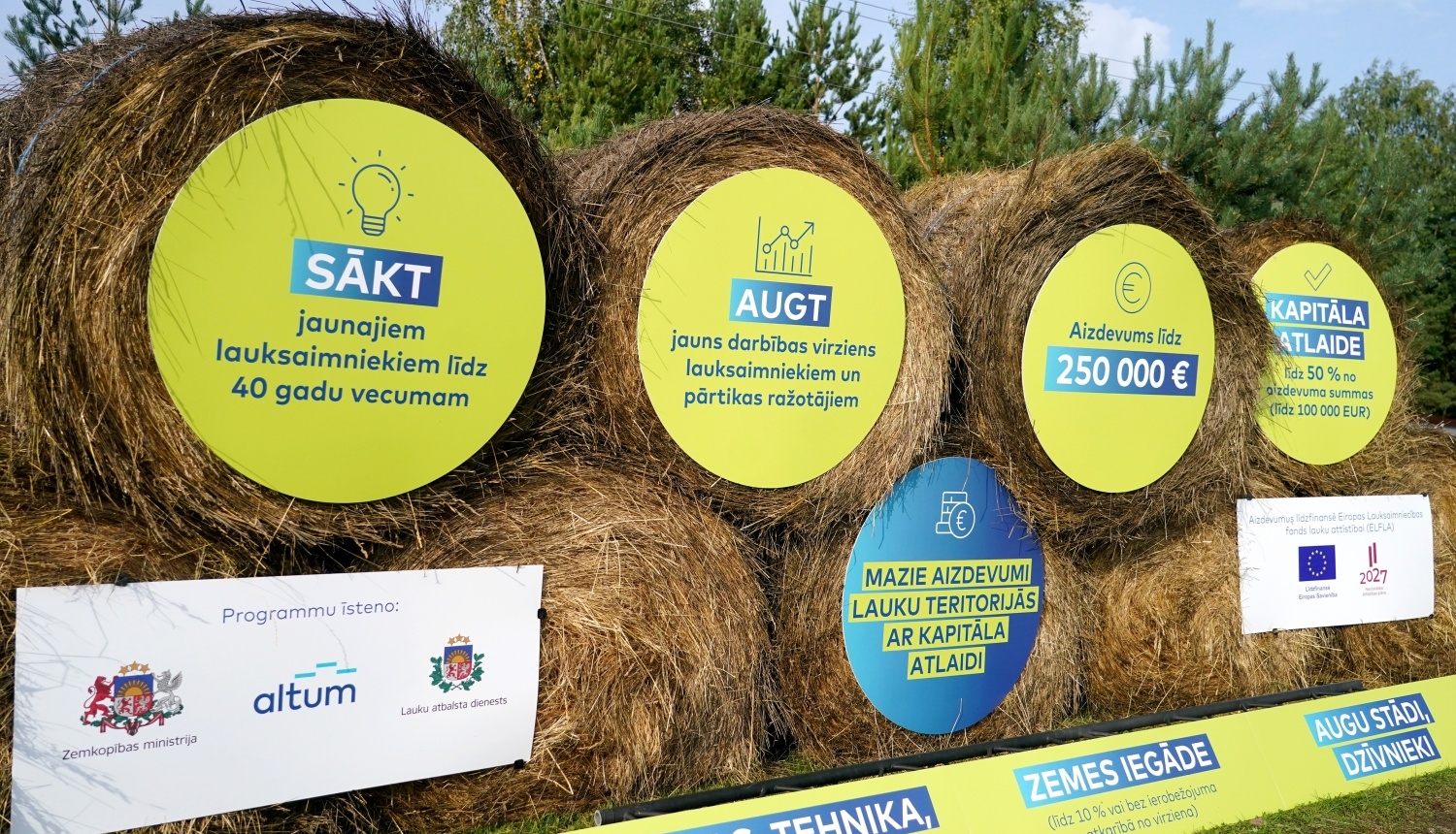 Siena ruļļi, kuru galos piestiprinātas apaļas reklāmas plāksnes par aizdevumu programmu