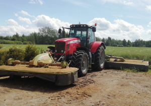 Sarkans traktors ar pļaujmašīnām stāv lauka malā