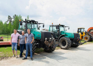 SIA Jāņlejas saimnieki stāv pie zaļa traktora, fonā vēl viens zaļš traktors un tālāk dzeltens traktors
