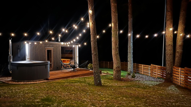 Namiņš naktī starp priedēm ar iekārtām lampiņām