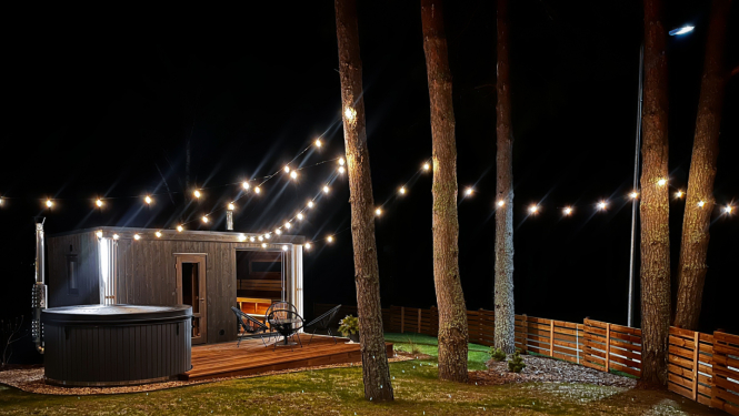 Namiņš naktī starp priedēm ar iekārtām lampiņām