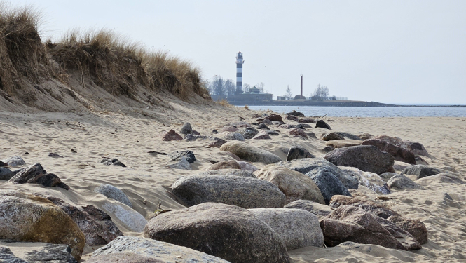 Jūras krasts, priekšplānā akmeņaina pludmale, tālumā bāka