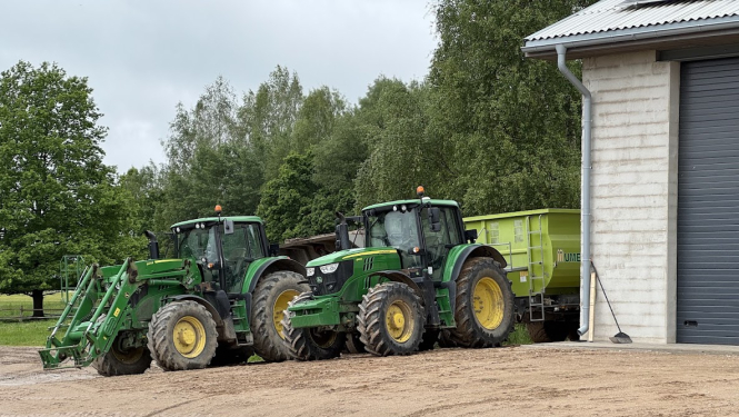 Divi traktori stāv aiz ēkas stūra