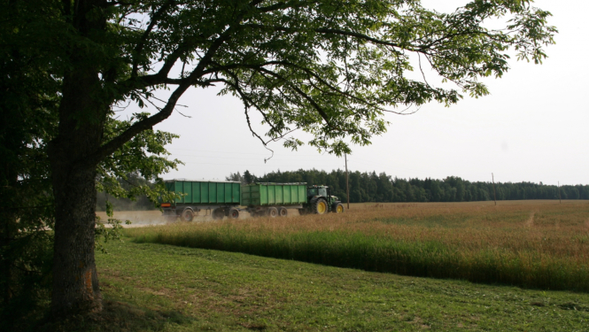 Traktors ar piekabi ved ražu pa lauku ceļu