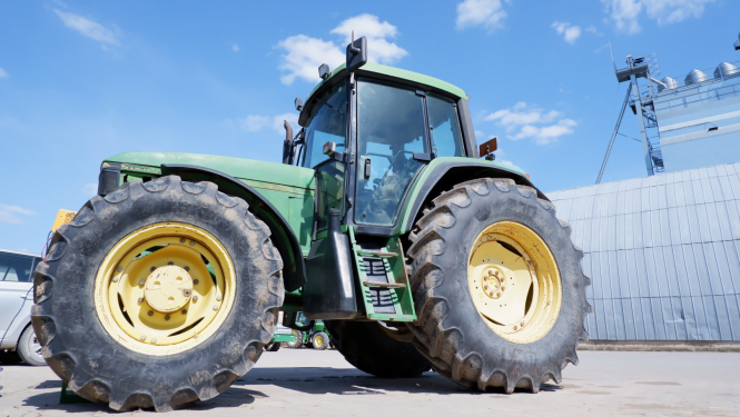 zaļš traktors no sāna, fonā metāla angārs