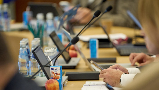 Galda virsmas ar tehniku no valdības sēdes, kā arī uz galda piena paciņas un āboli