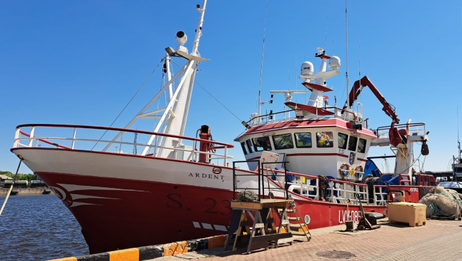 Sarkans ar baltu zvejas kuģis pietauvots ostā