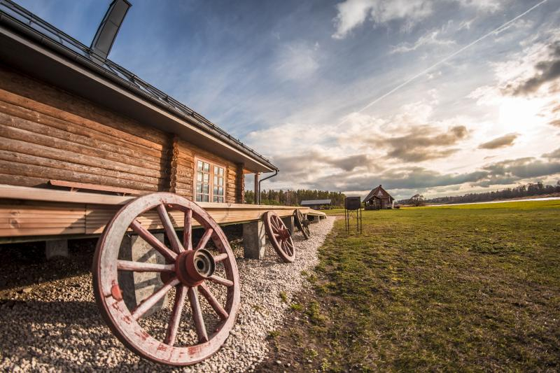 Lauku ēkas sāns ar pieslietu koka ratu riteni