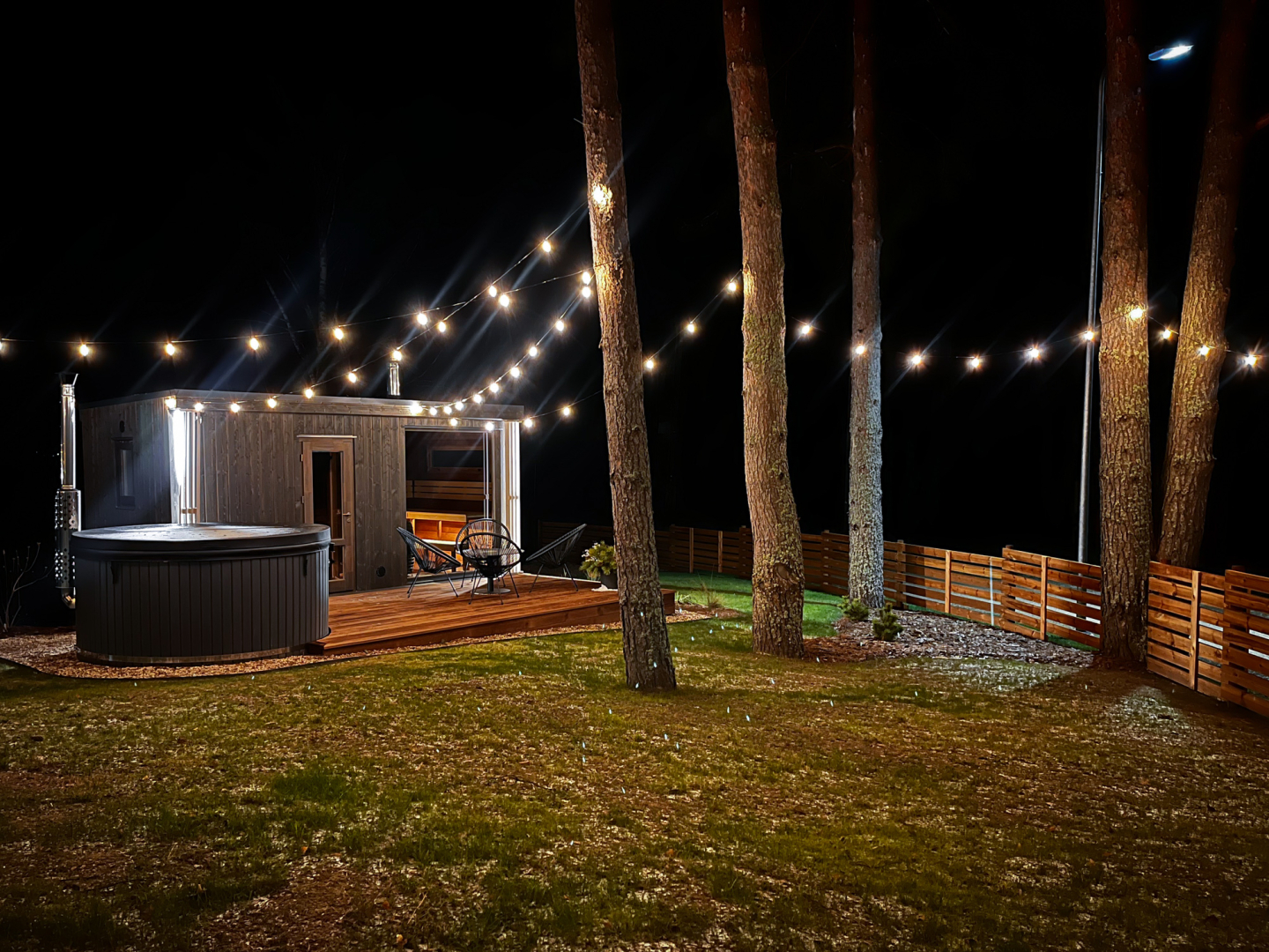 Namiņš naktī starp priedēm ar iekārtām lampiņām