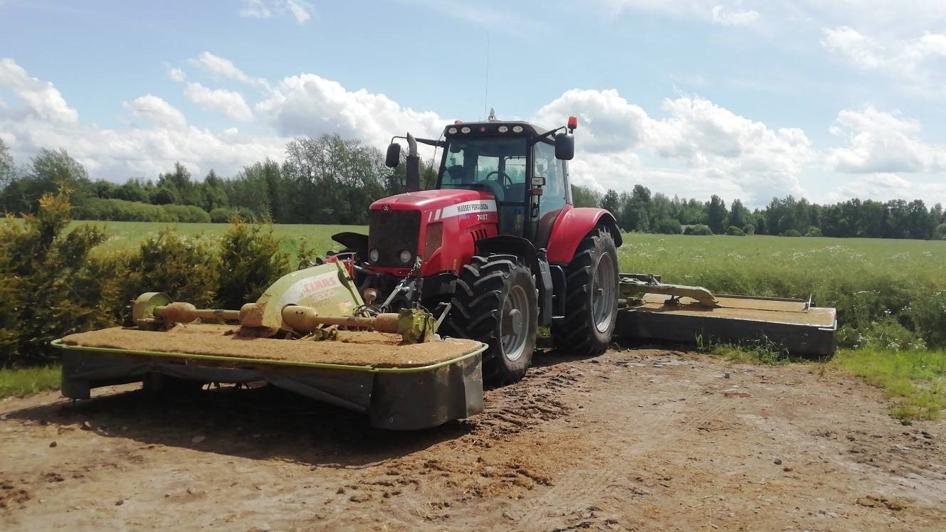 Sarkans traktors ar pļaujmašīnām stāv lauka malā