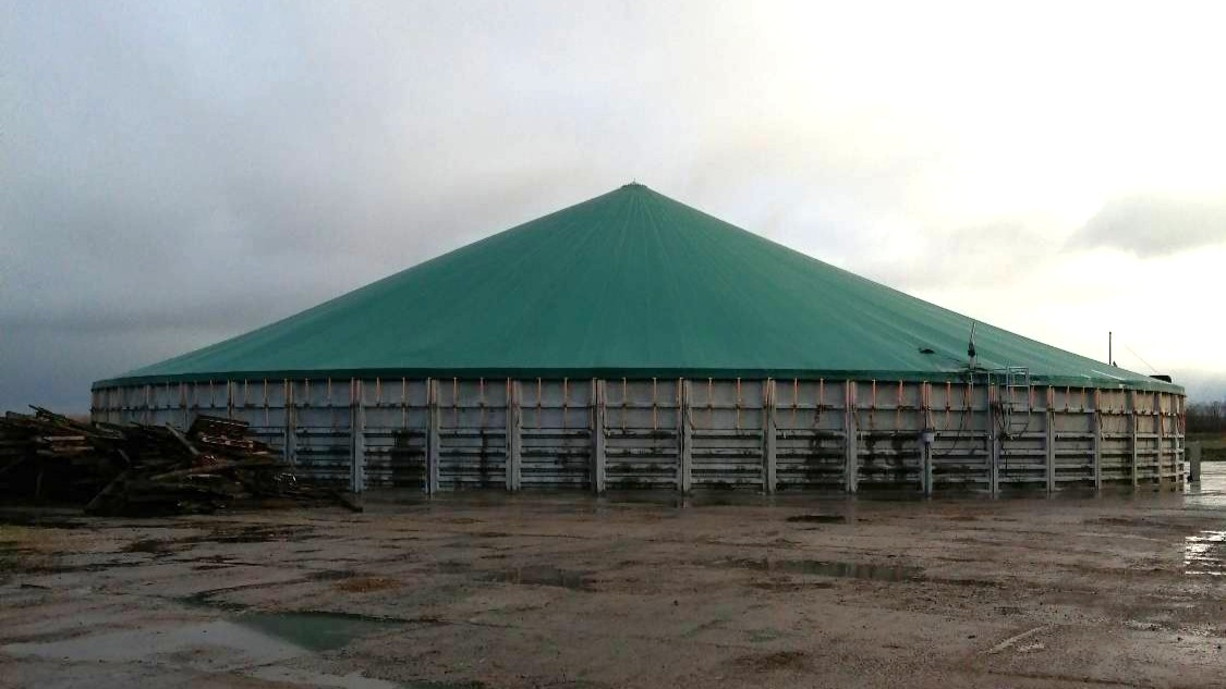 Šķidrmēslu krātuve, apaļa būve ar zaļu trīsstūrveida jumtu