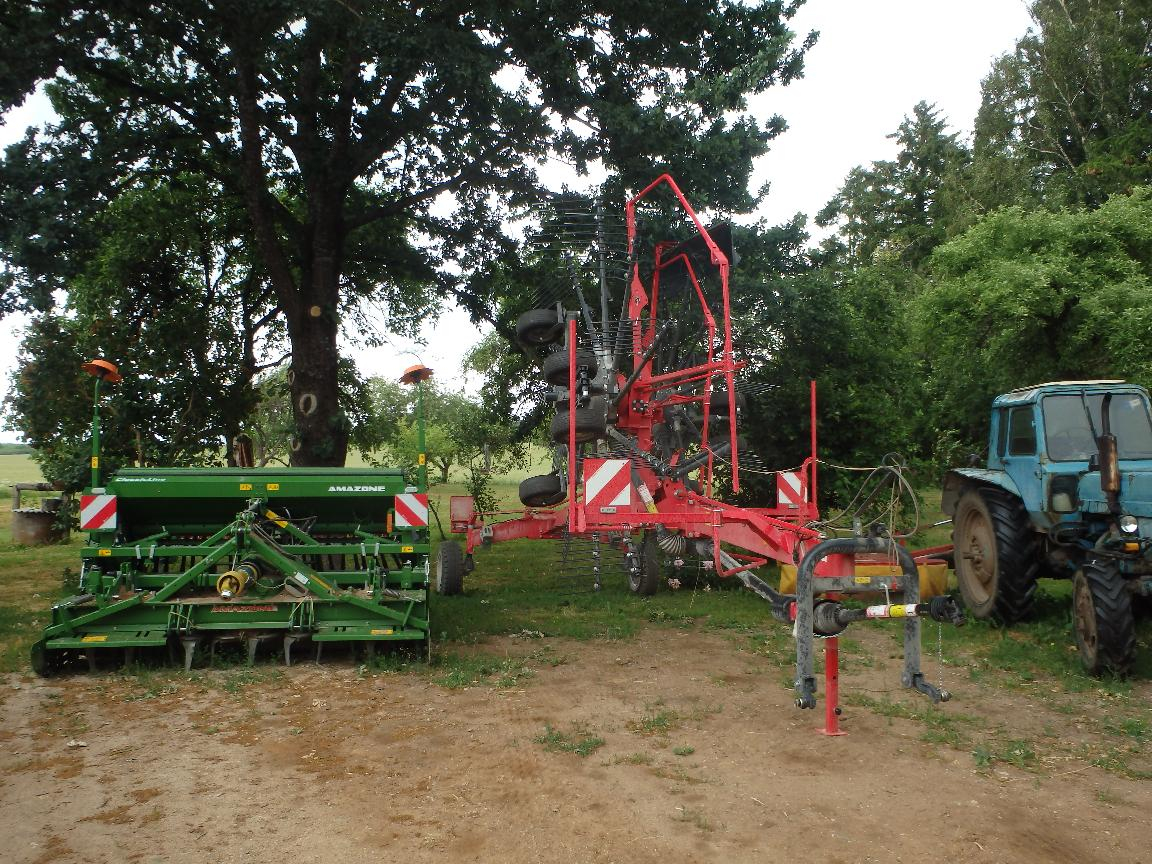 Sarkans un zaļš traktora agregāts stāv blakus zilam traktoram