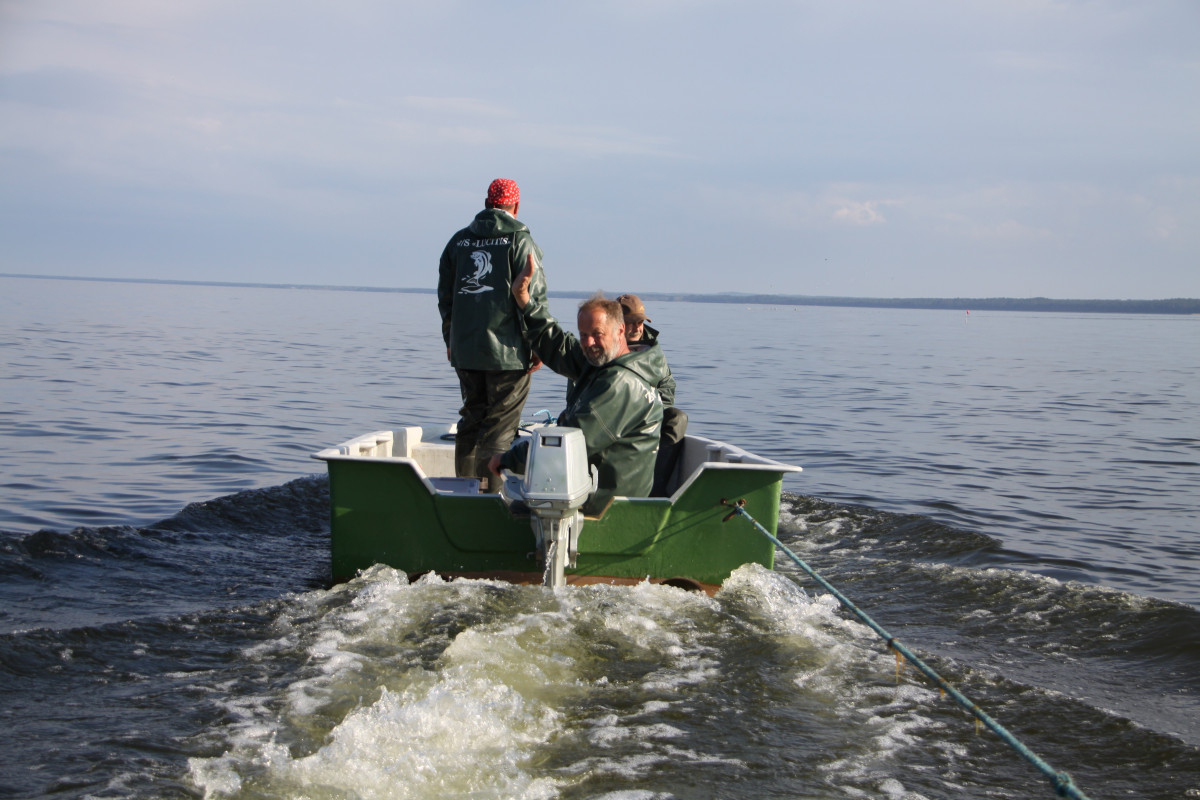Trīs zvejnieki prombraucošā laivā 