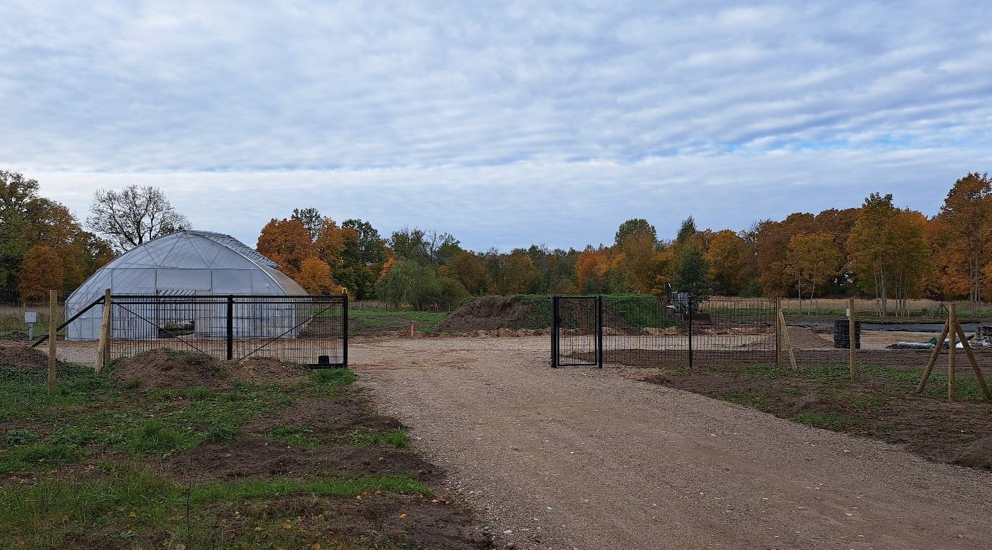 Iebraucamais ceļš un grantēts laukums, kurā atrodas siltumnīca