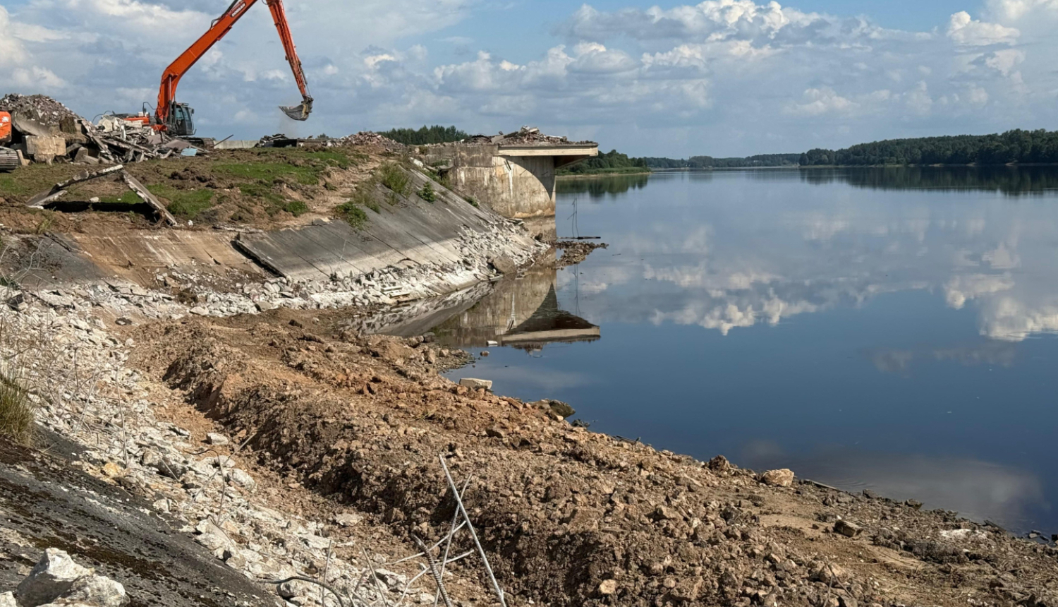 augsts upes krasts uz kura stāv sarkans ekskavators