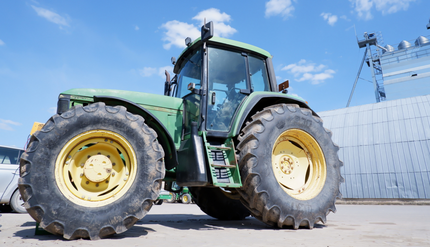 zaļš traktors no sāna, fonā metāla angārs