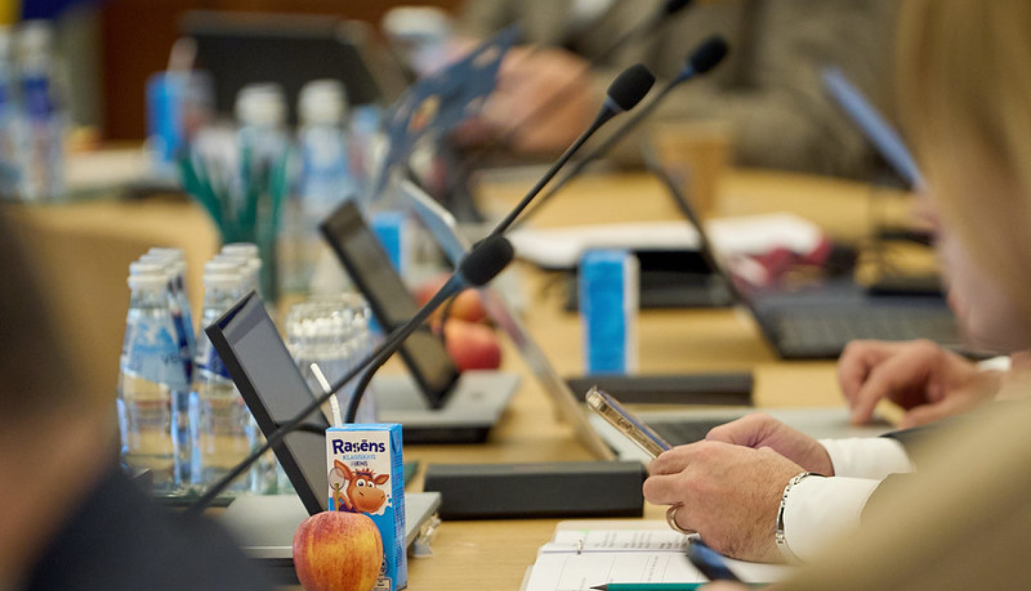 Galda virsmas ar tehniku no valdības sēdes, kā arī uz galda piena paciņas un āboli