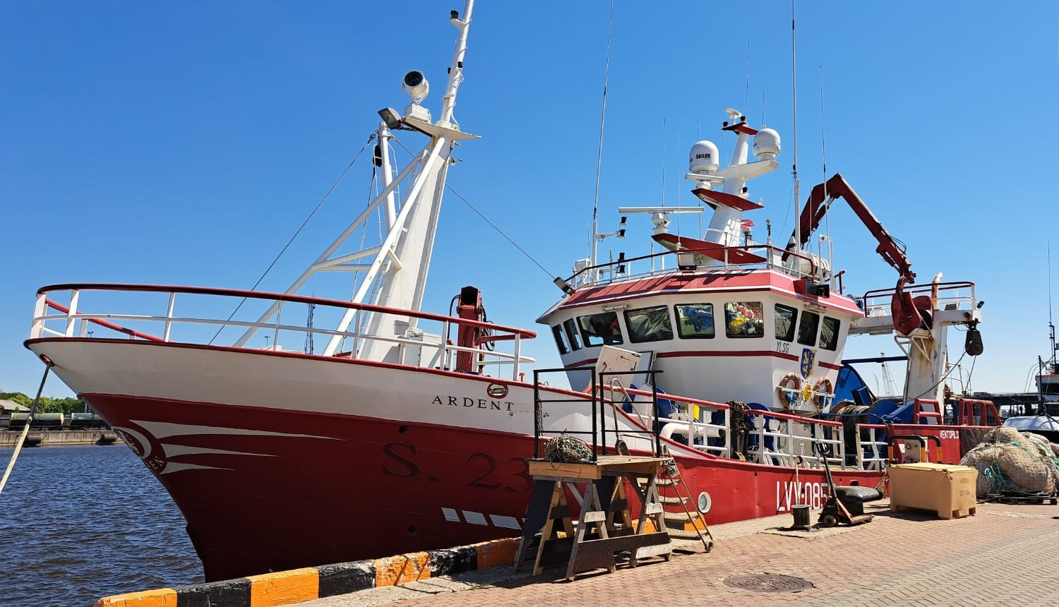 Sarkans ar baltu zvejas kuģis pietauvots ostā