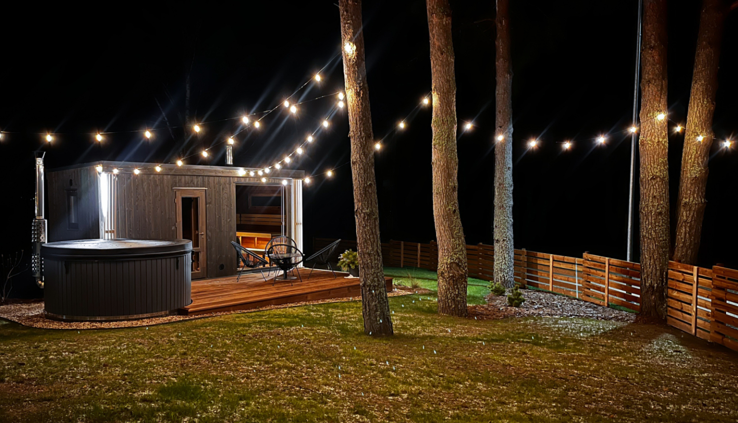 Namiņš naktī starp priedēm ar iekārtām lampiņām